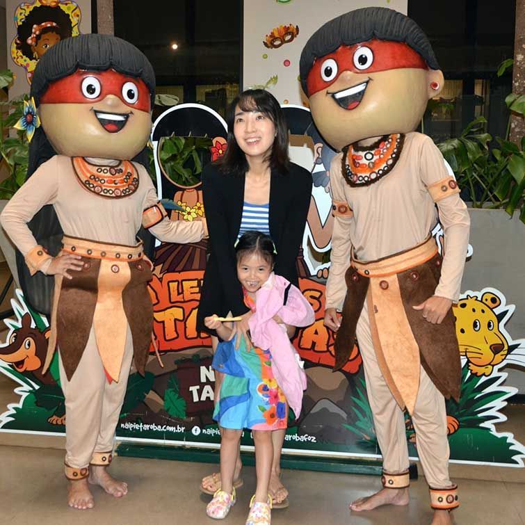 Mulher e criança posam com dois mascotes de desenho animado em um evento.