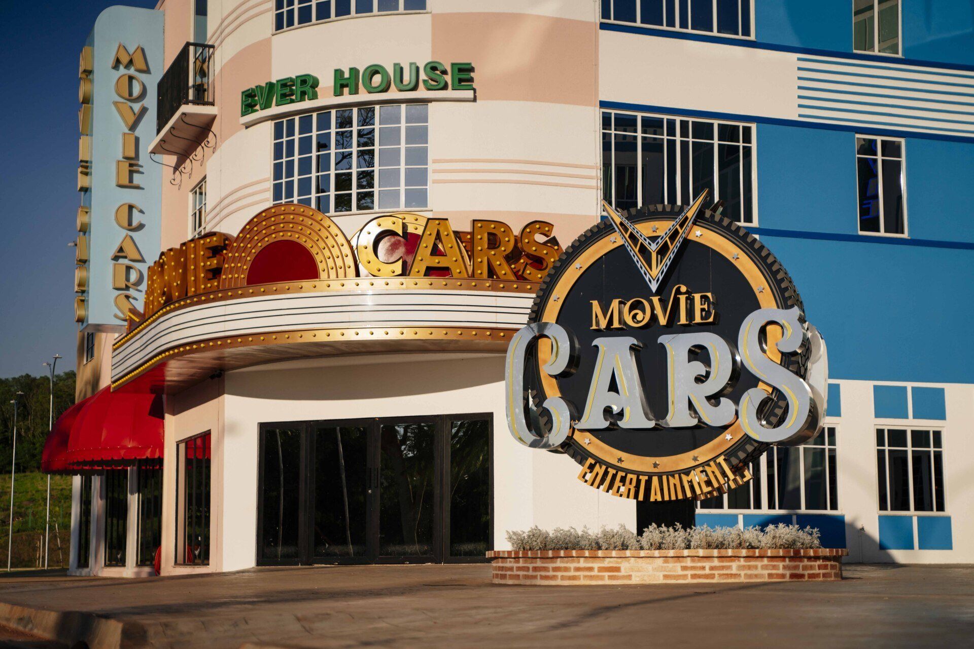 Prédio do Movie Cars com sinalização dourada e prateada; exterior azul, branco e bege.