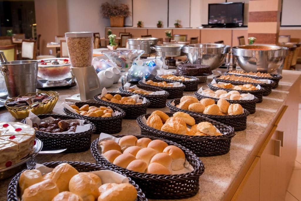 Buffet de café da manhã com diversos tipos de pães, cereais e outros alimentos dispostos em cestas.