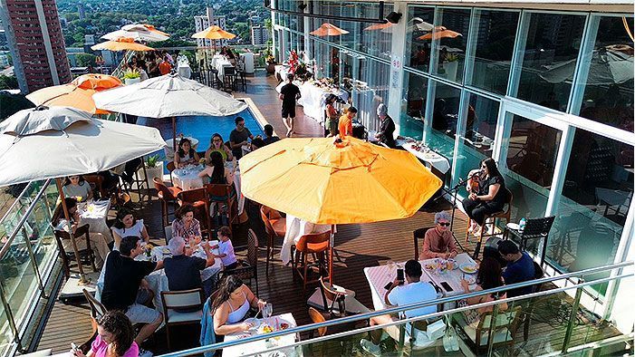Restaurante no terraço: pessoas jantando em mesas com guarda-sóis. Vista da cidade.