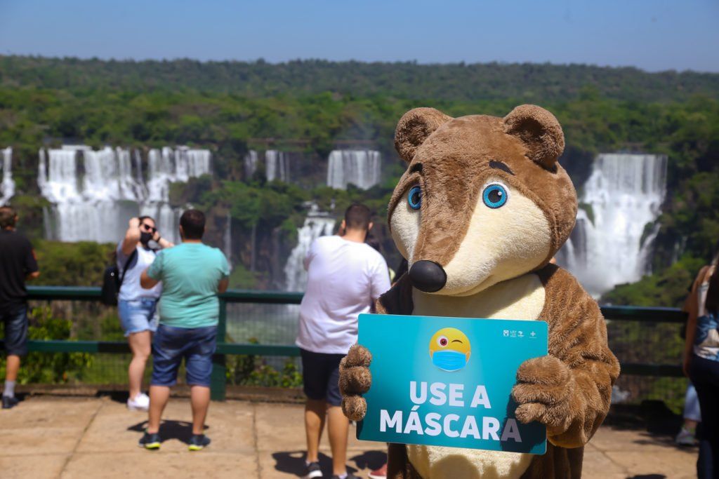 Um mascote com uma placa de máscara está nas Cataratas do Iguaçu, incentivando o uso de máscaras.