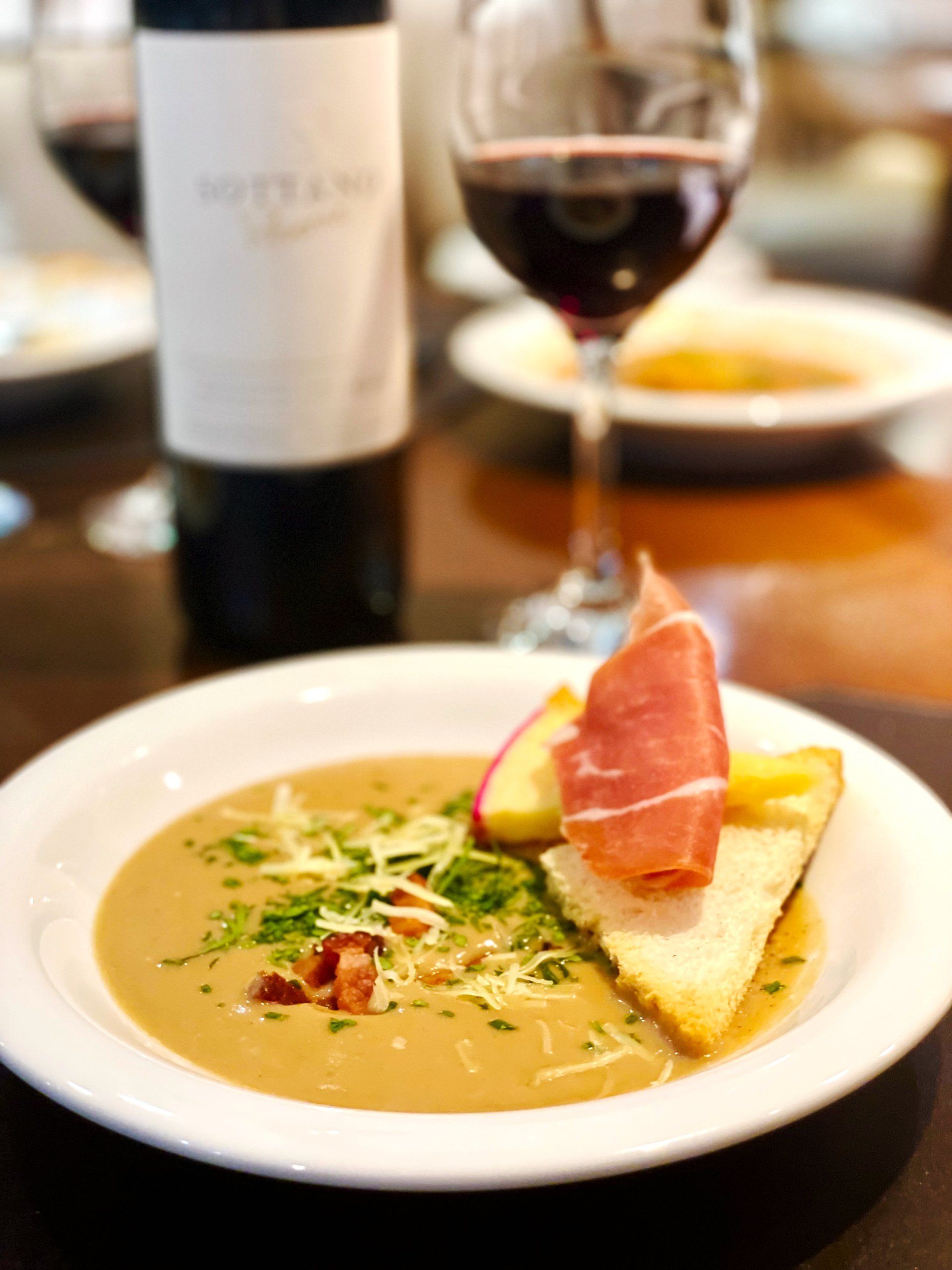 Sopa com presunto, maçã e pão torrado, servida com vinho tinto.