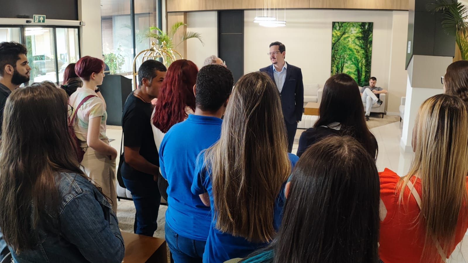 Um homem de terno fala com um grupo de jovens adultos em um saguão.