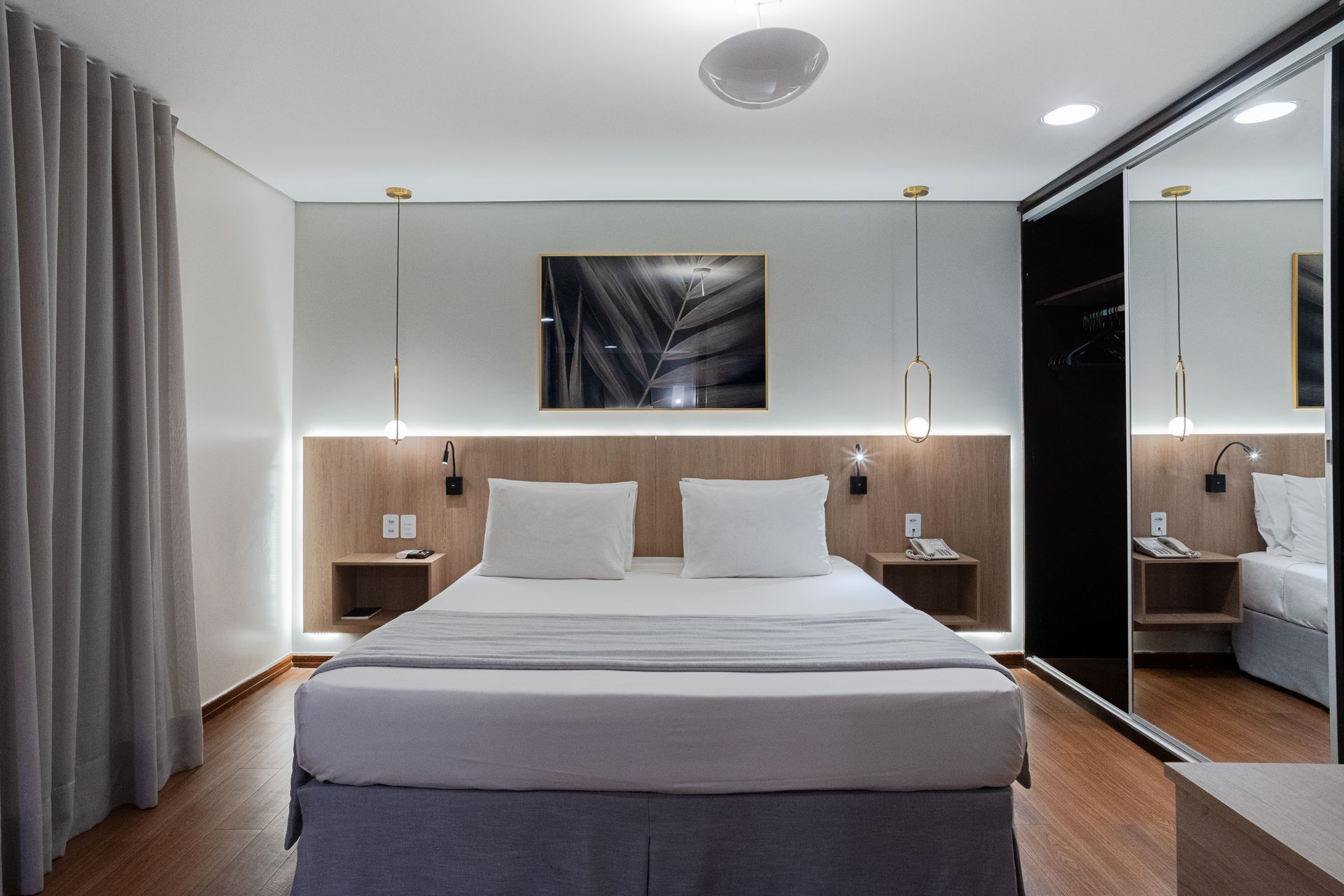 Quarto com cama de casal, mesas de cabeceira e um amplo armário com porta espelhada.