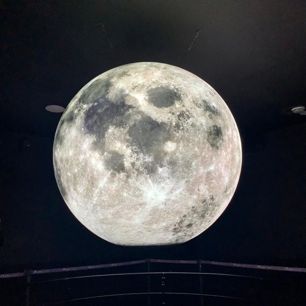 Lua gigante iluminada suspensa no teto contra um fundo escuro.