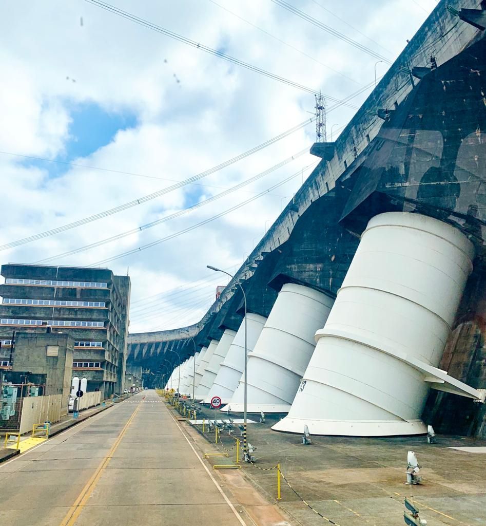 Uma barragem com estruturas de turbinas brancas. Uma estrada corre ao lado de um prédio sob um céu nublado.