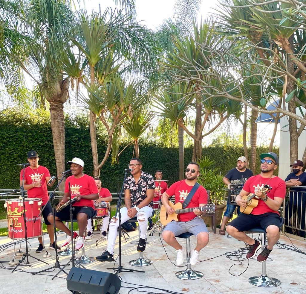 Uma banda de músicos tocando ao ar livre; eles vestem camisas vermelhas, tocam instrumentos e cantam.