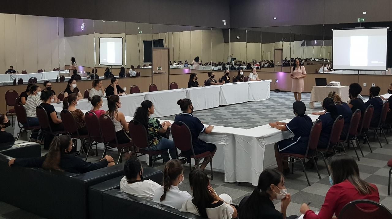Uma sala de conferências com um palestrante se dirigindo a uma plateia sentada em mesas.