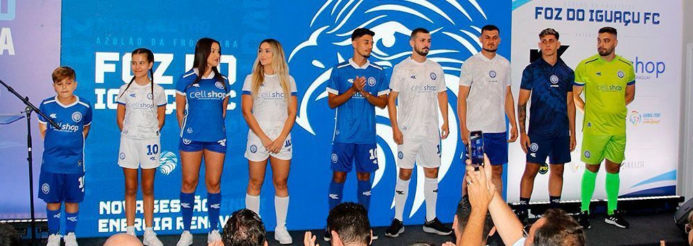 Pessoas no palco com uniformes de futebol. Cores azul, branco e verde. Texto 