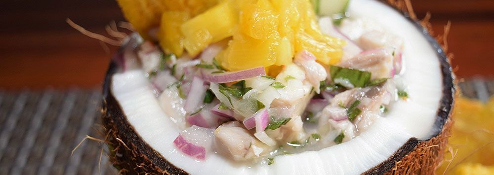 Close-up de ceviche em casca de coco, decorado com frutas amarelas picadas.