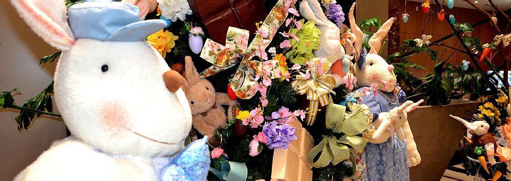 Exposição de Páscoa com coelhinhos de pelúcia, flores e decorações.