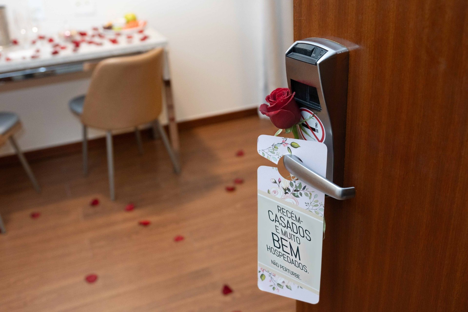 Visão noturna de um hotel com janelas iluminadas, um estacionamento e luzes da cidade ao fundo.