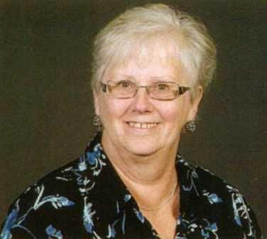 A woman wearing glasses and a floral shirt is smiling for the camera.