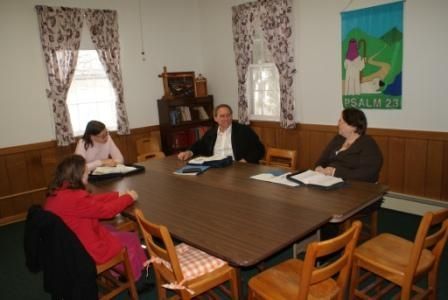 A group of people are sitting around a table with psalm 27 on the wall behind them