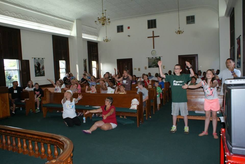 A group of children are dancing in a church with a cross on the wall
