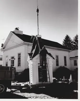 A black and white photo of a man on a ladder in front of a white building