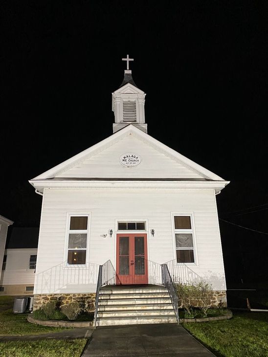 A white church with a red door and stairs at night.