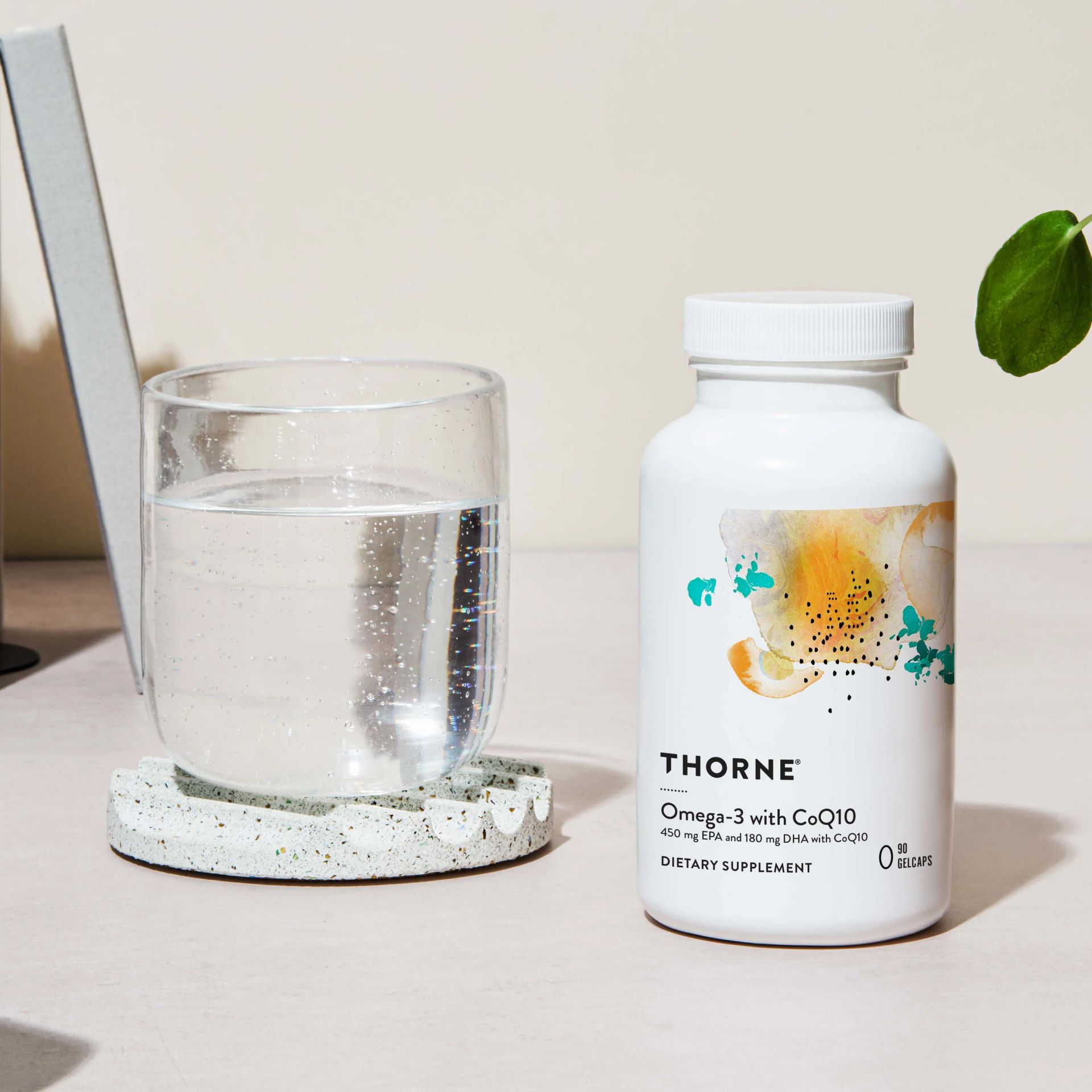 Bottle of Thorne Omega-3 with CoQ10 and a glass of water on a desk.
