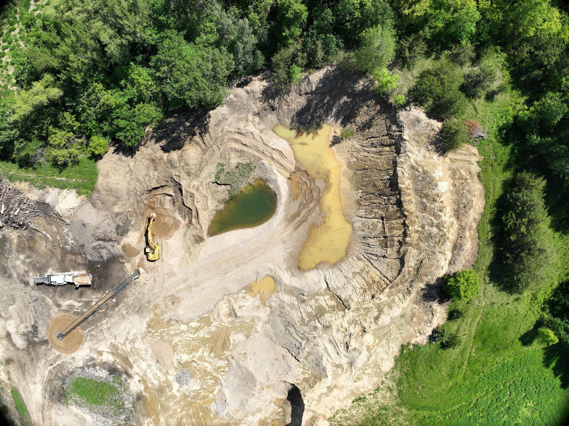 An aerial view of a construction site with a pond in the middle of it surrounded by trees.