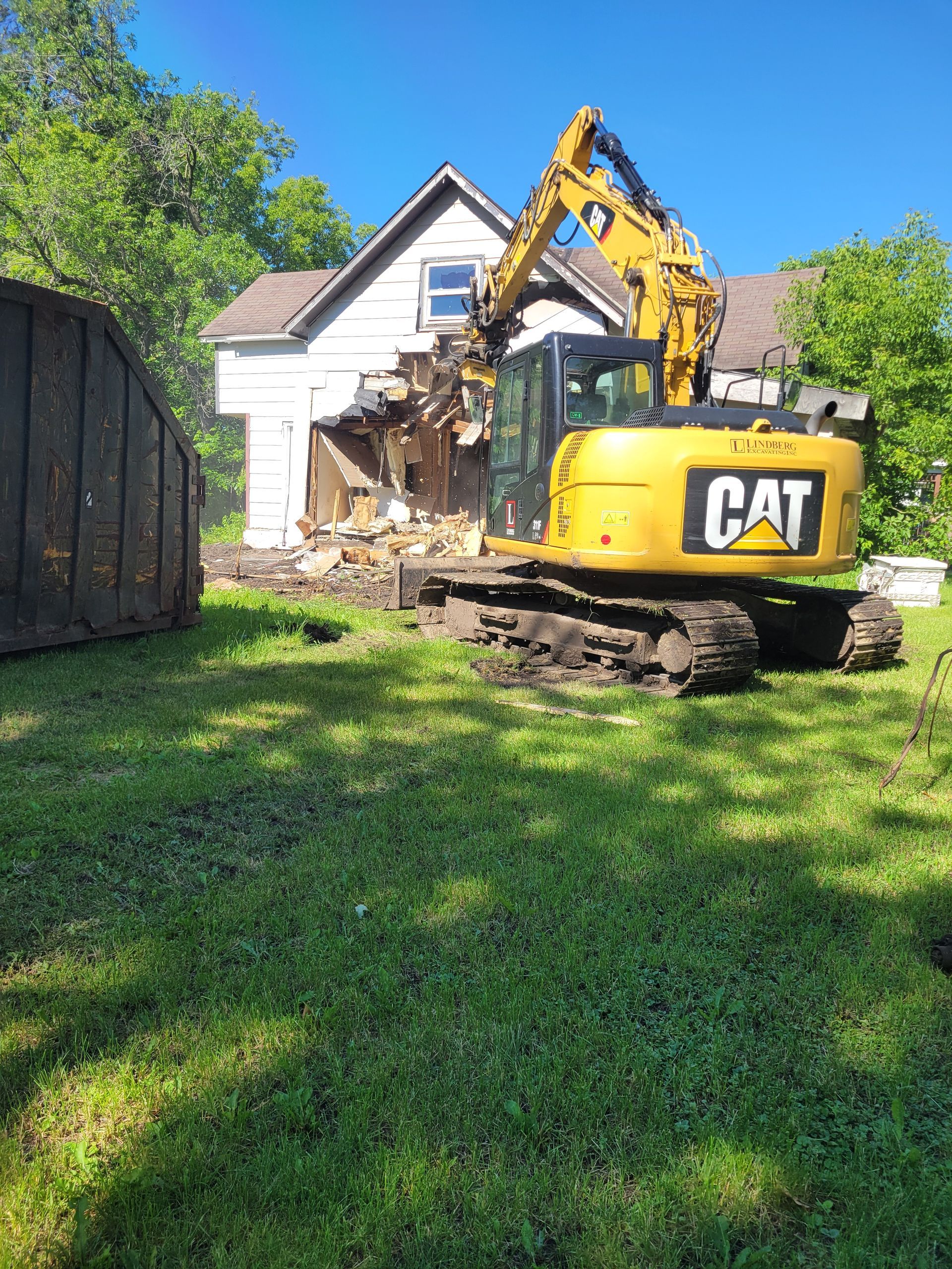 A cat excavator is demolishing a house in a yard.
