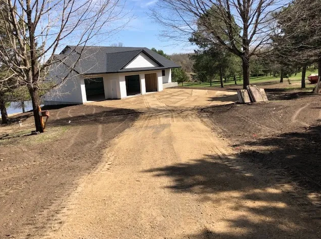A dirt road leading to a white house surrounded by trees.