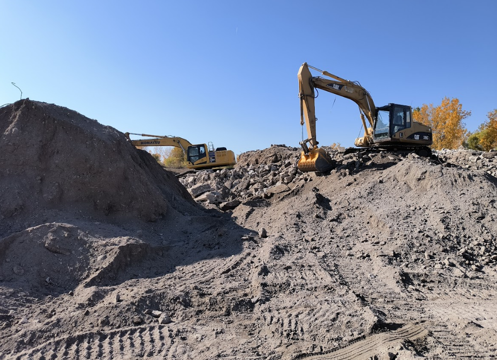 Two excavators are working on a pile of dirt.