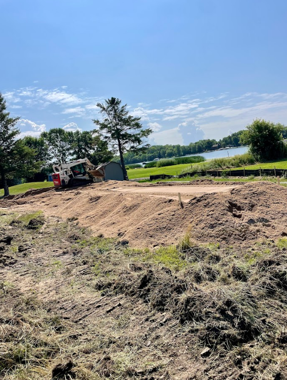 A bulldozer is moving dirt in a field next to a lake.