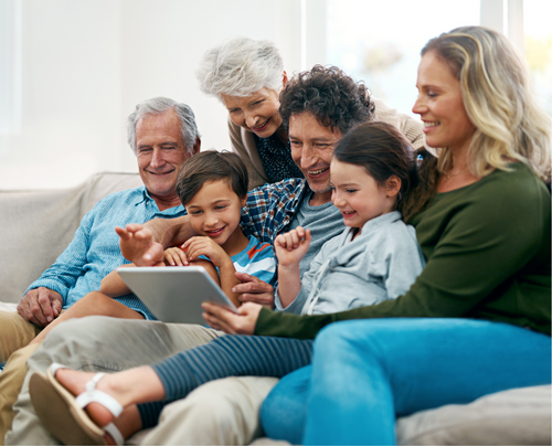 a family is sitting on a couch looking at a tablet.
