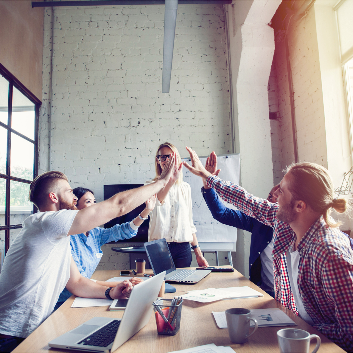 a group of people are giving each other a high five while sitting around a table .