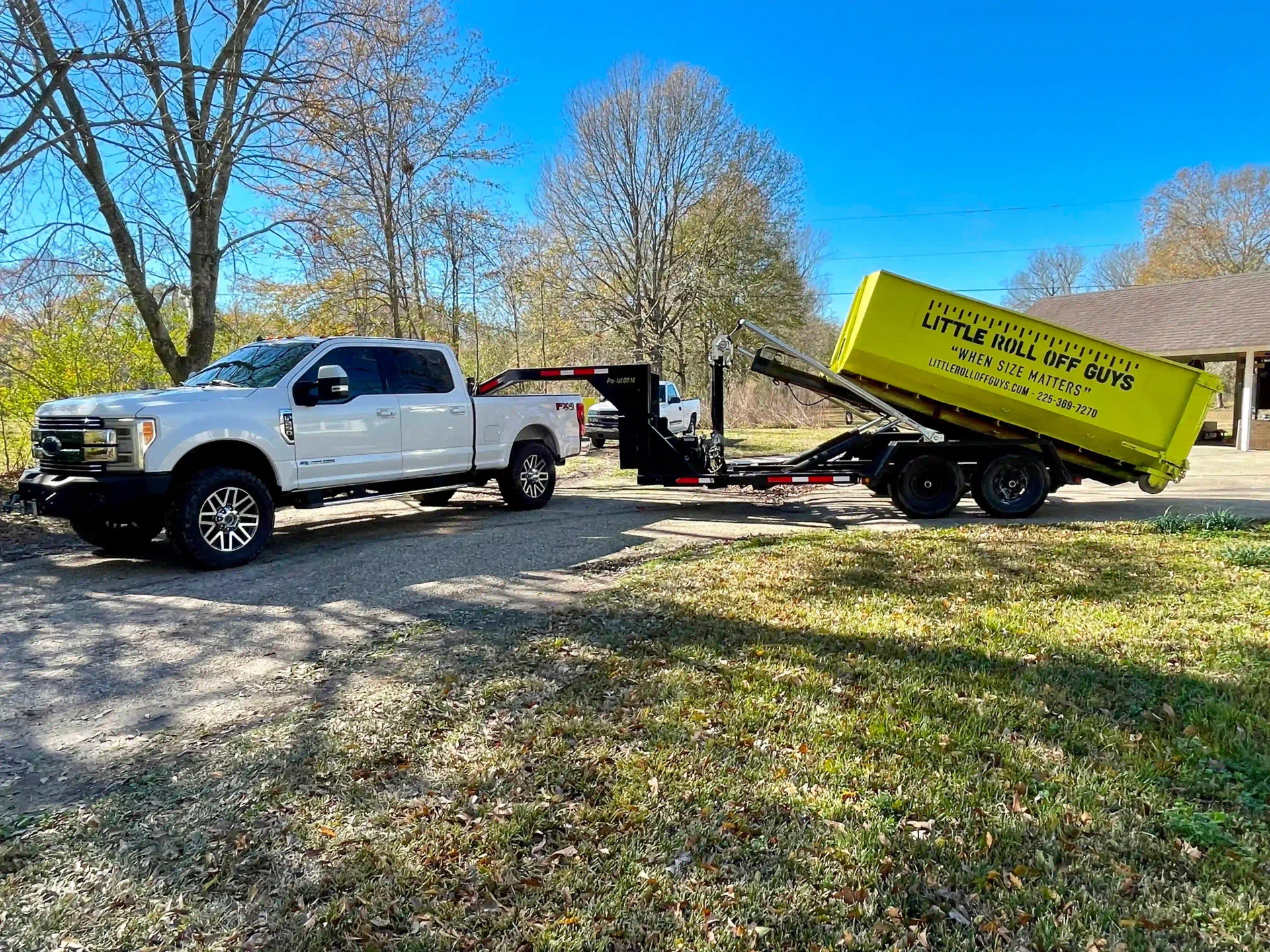 A white truck is towing a yellow dumpster on a trailer.
