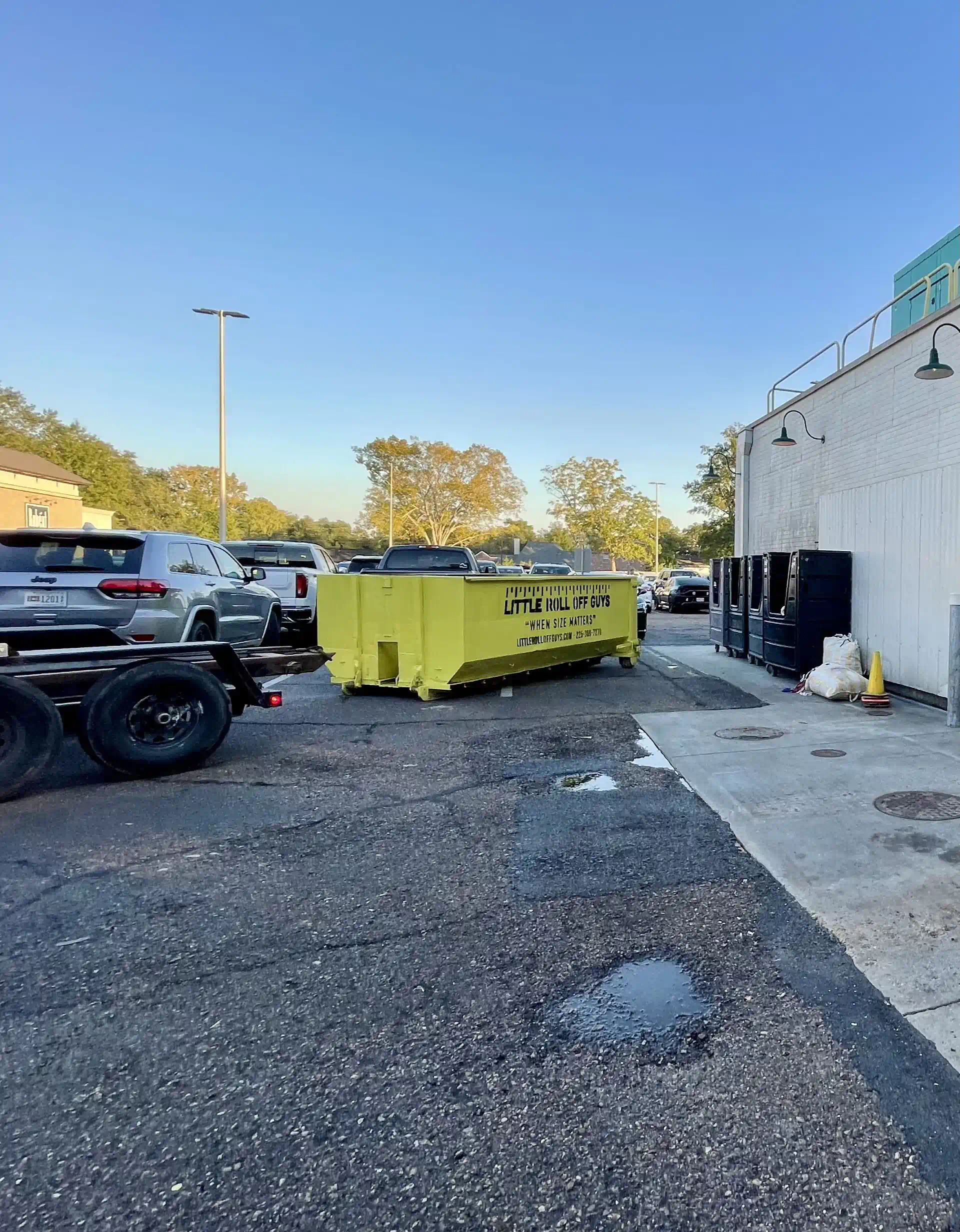 A yellow dumpster is parked in a parking lot next to a truck.