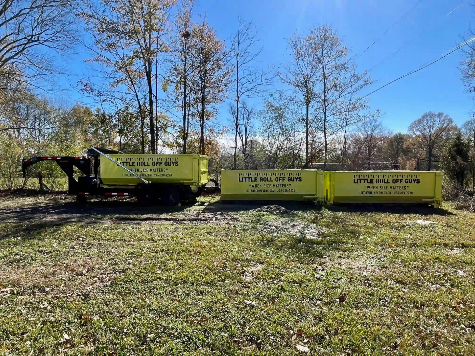 A dumpster truck is parked in a grassy field.