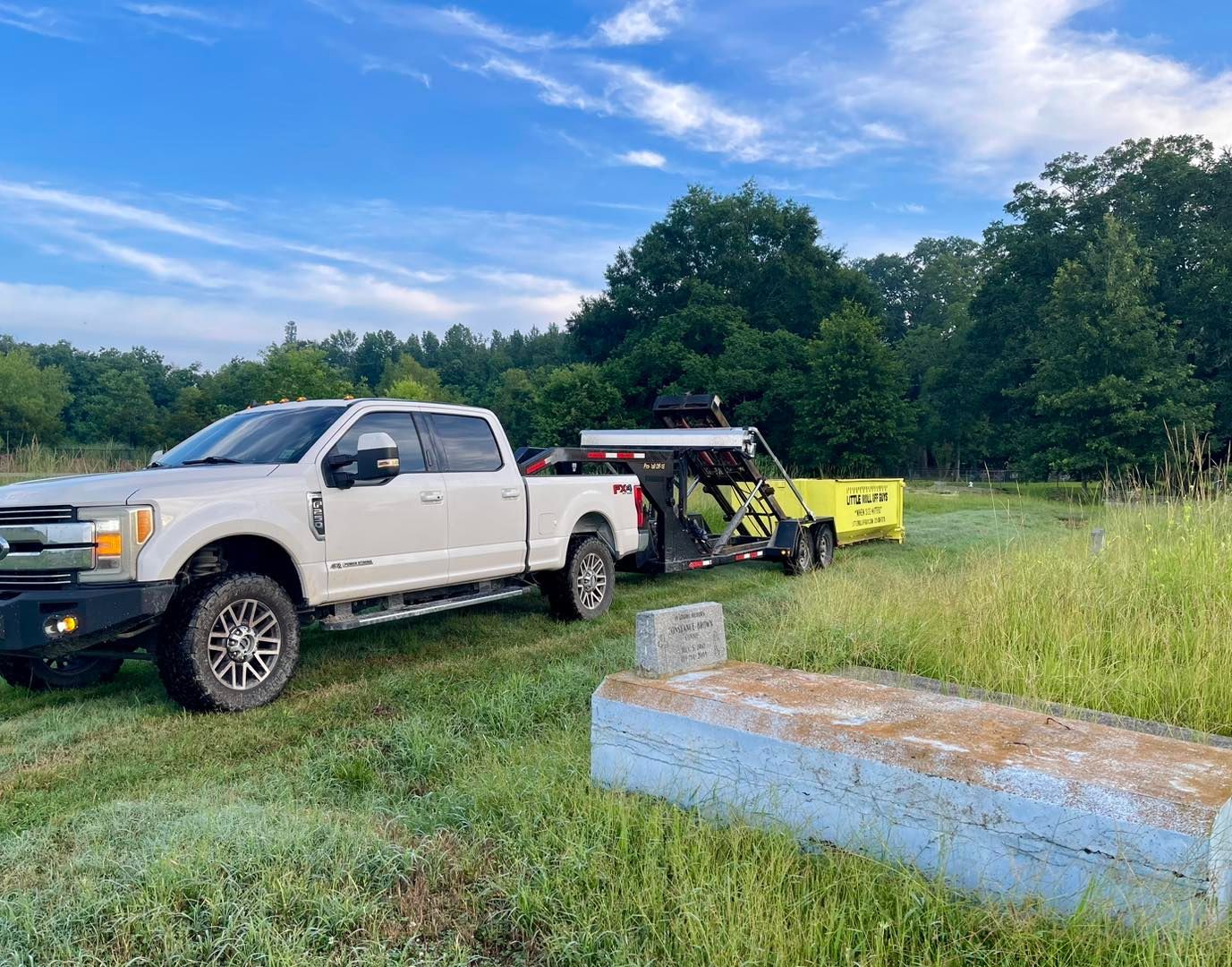 A white truck is towing a yellow trailer in a grassy field.