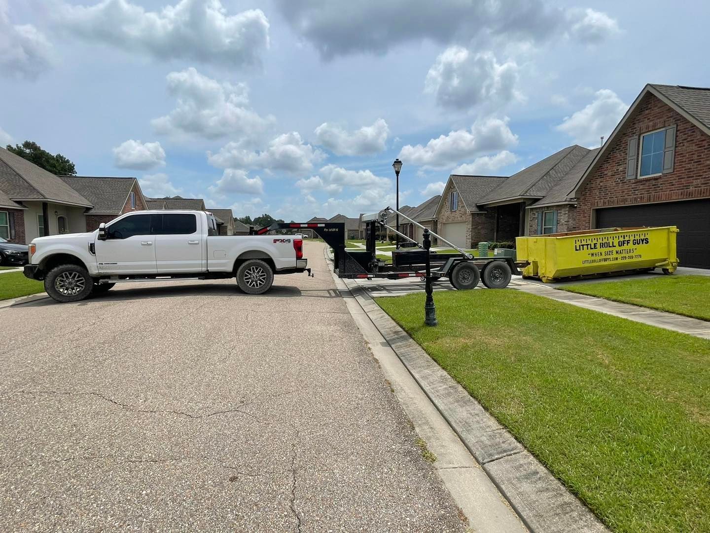A white truck is towing a yellow dumpster down a driveway.