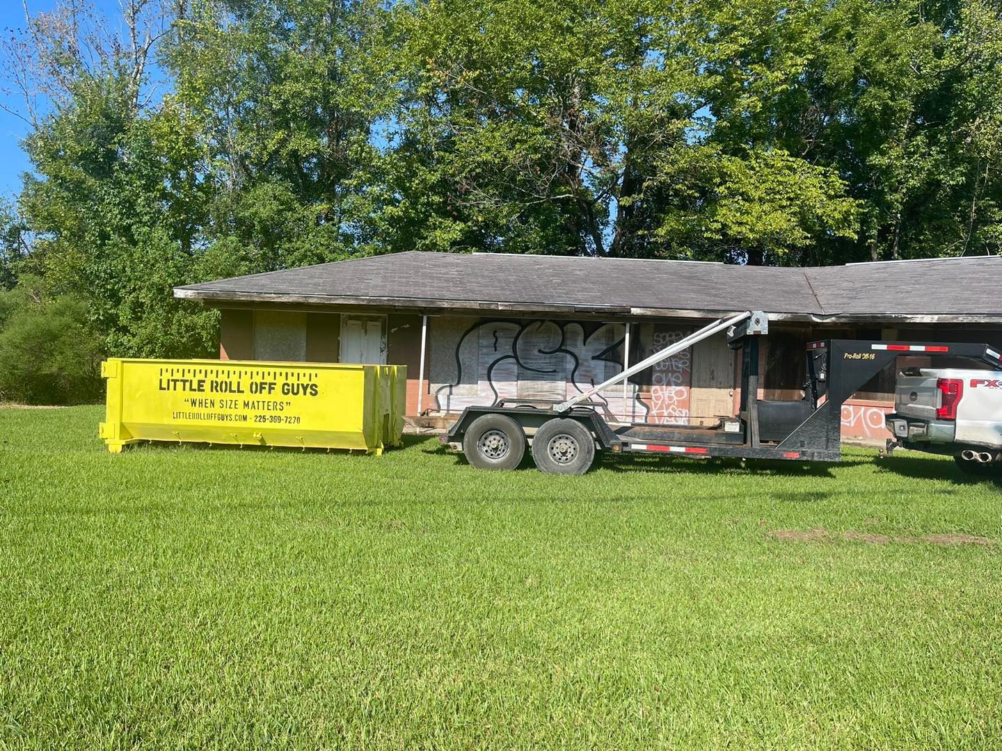 A dumpster is being towed by a truck in front of a house.