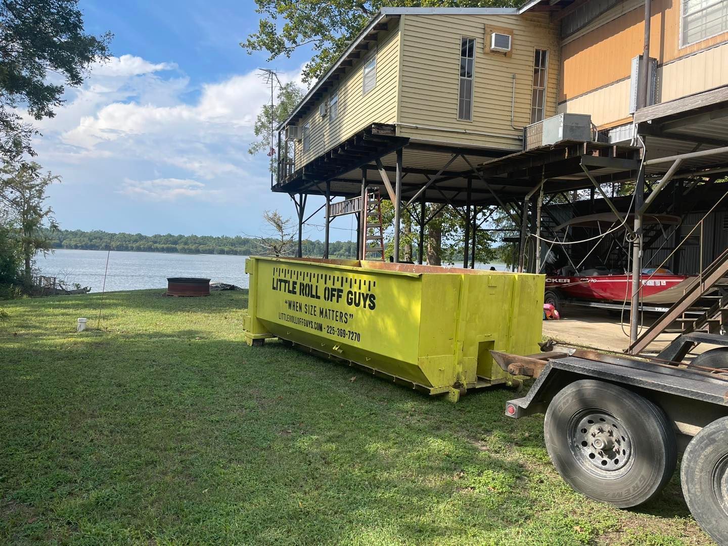 A yellow dumpster is sitting on top of a trailer in front of a house.