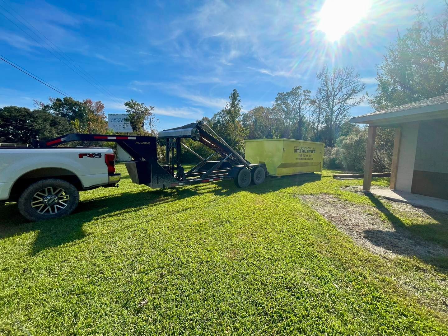 A truck is towing a dumpster in a grassy field.