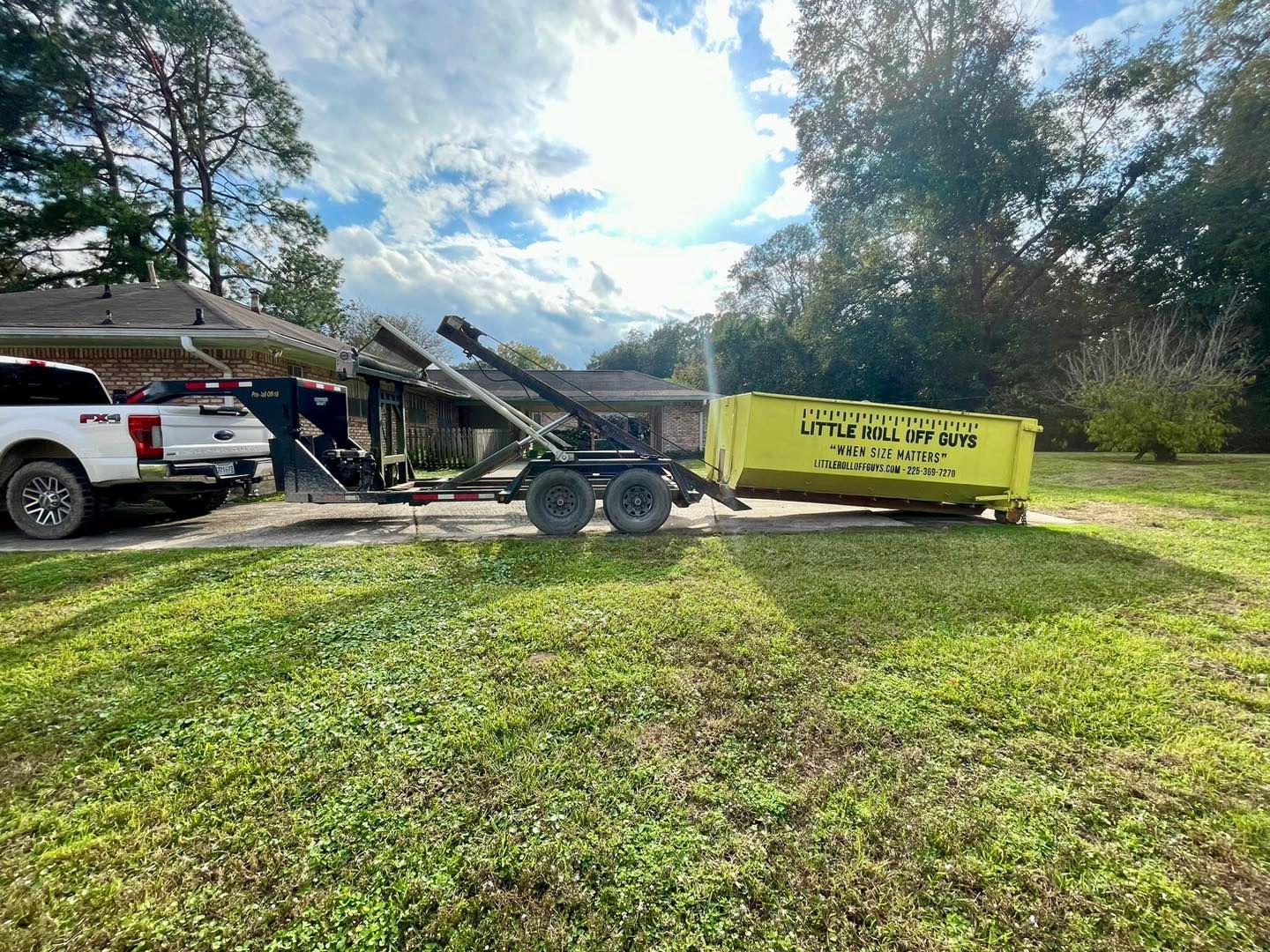A dumpster is being towed by a truck in a yard.