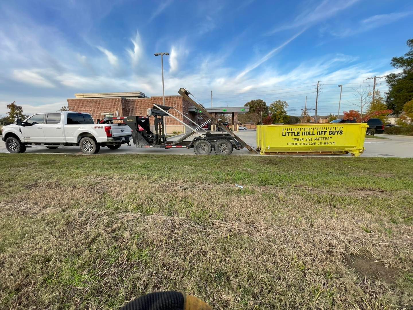 A dumpster is being towed by a truck in a parking lot.