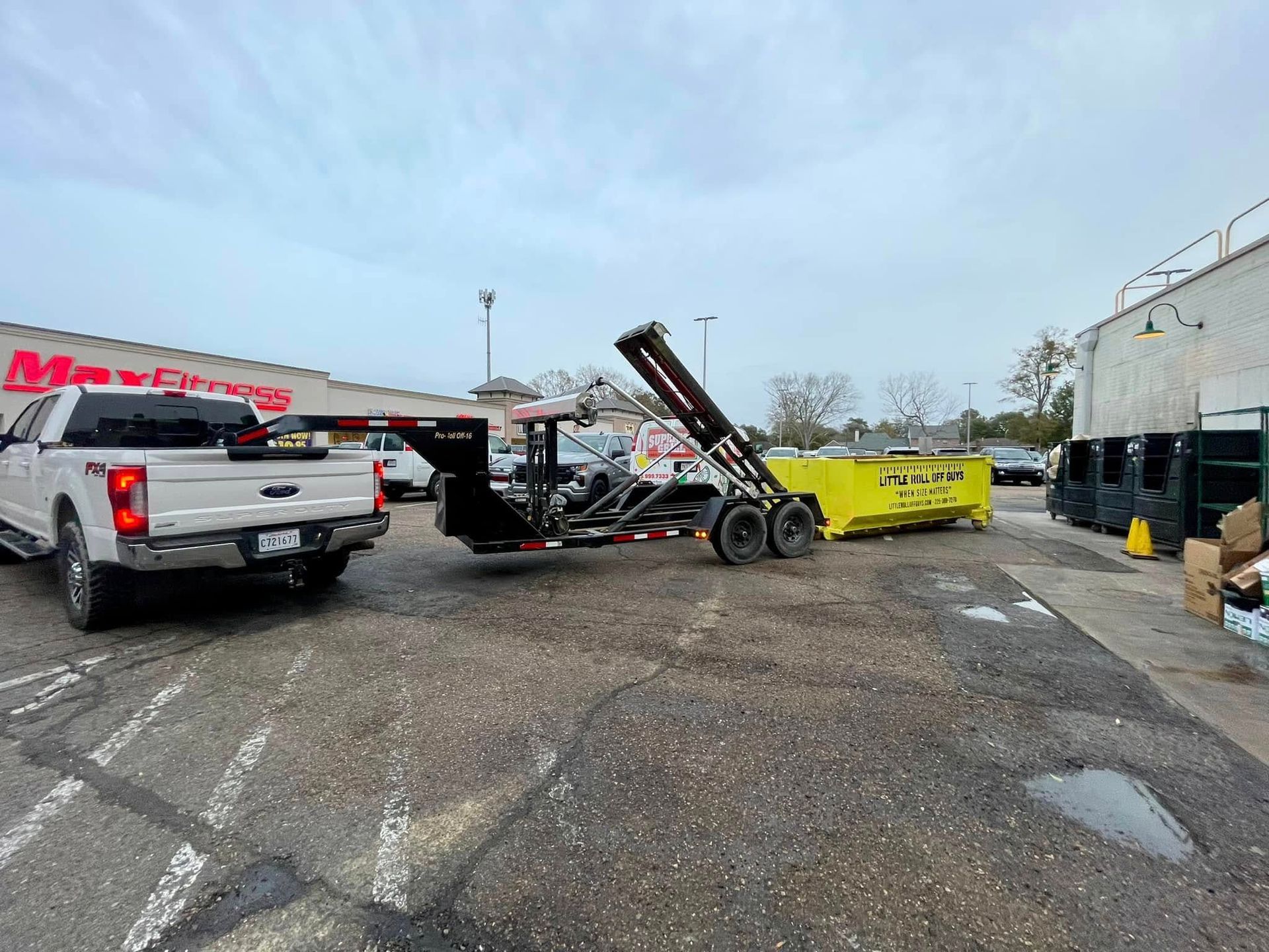 A dumpster is being towed by a truck in a parking lot.