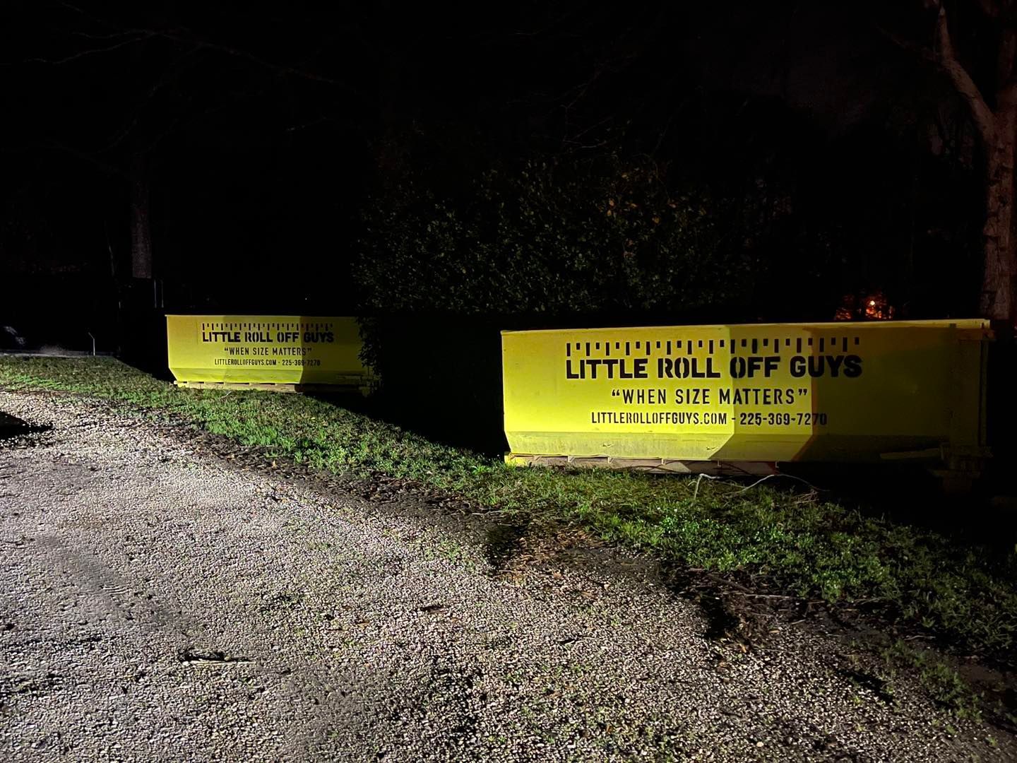 A couple of yellow dumpsters are parked on the side of a road at night.