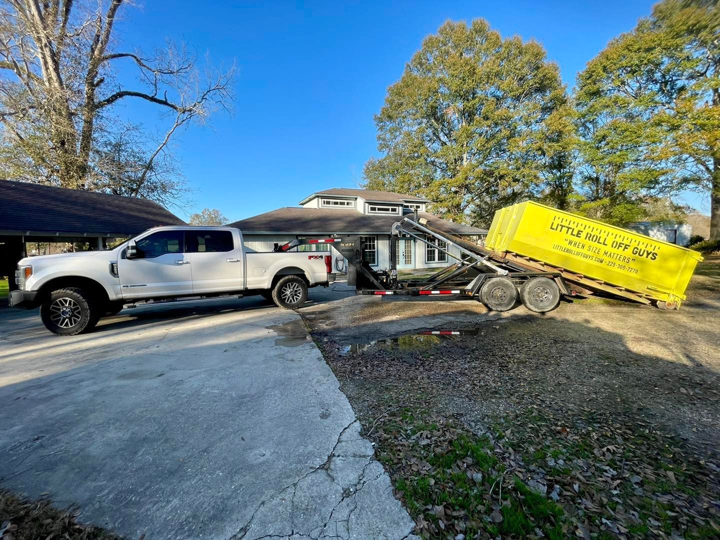 A white truck and a yellow dumpster are parked in front of a house.