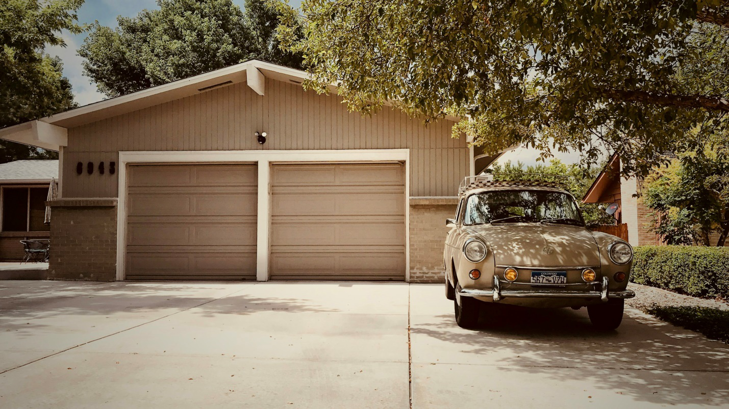 A car is parked in front of a house with two garage doors.