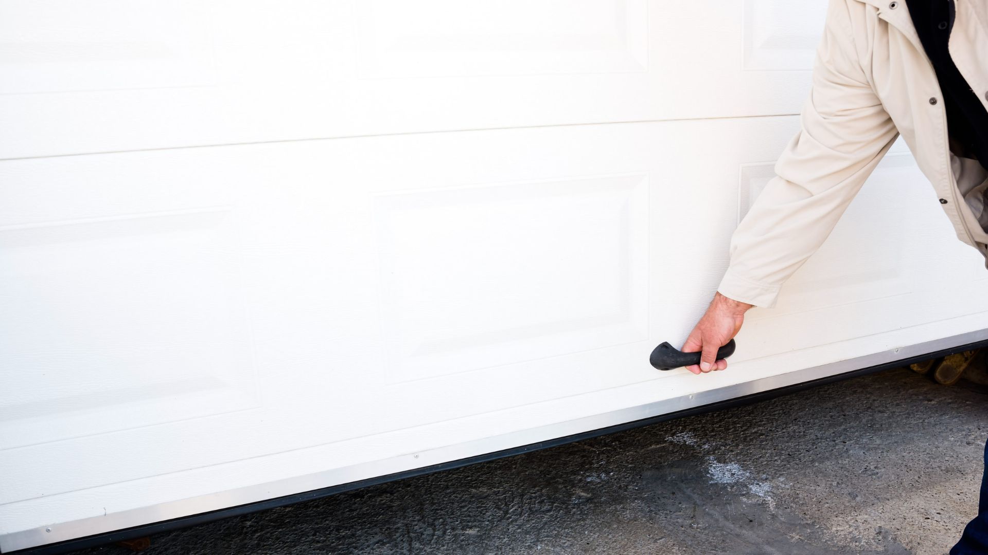 A man is opening a white garage door with a black handle.