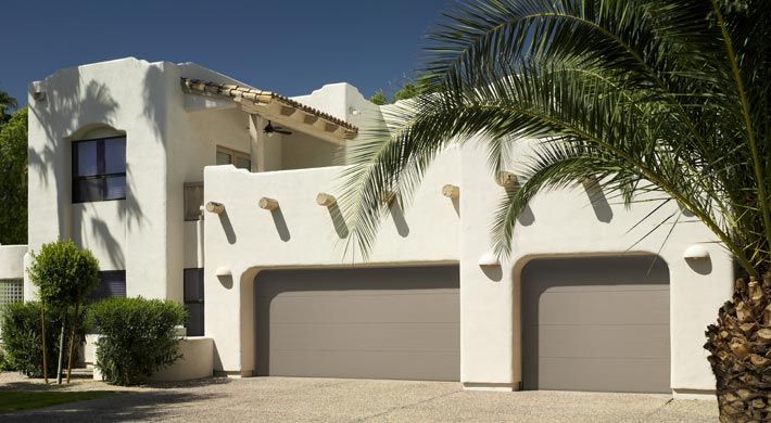 A white house with two garage doors and a palm tree in front of it.