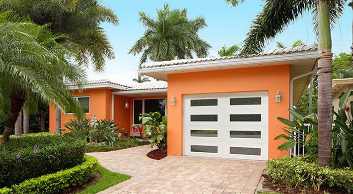 An orange house with a white garage door is surrounded by palm trees.