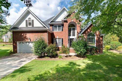 A large brick house with a white garage door is sitting on top of a lush green lawn.