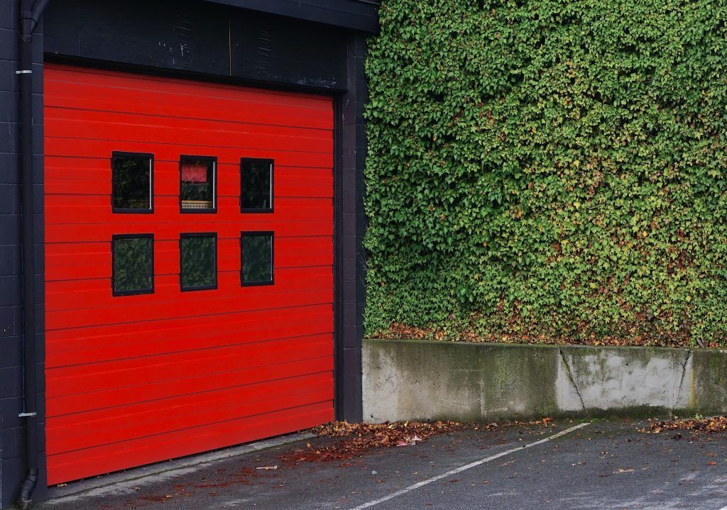A red garage door with a green hedge in the background