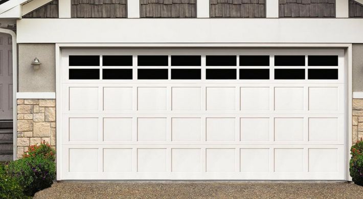 A white garage door with black windows is sitting in front of a house.