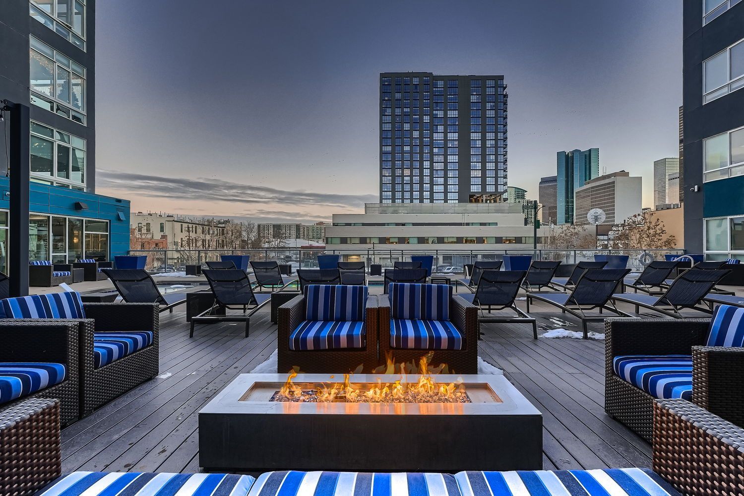 Rooftop lounge with fire pit, seating, and city skyline view. Blue and white striped cushions.